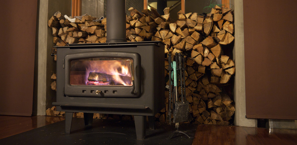 Burning wood stove with with pile of firewood